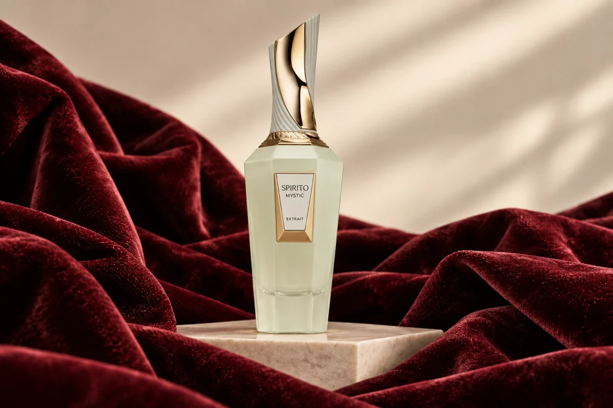 Illustration of a pale green Spirito Mystic Extrait bottle with a sculpted gold and white cap, on a marble block among burgundy velvet.